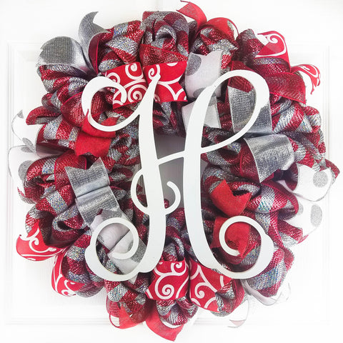 Red and silver Christmas mesh wreath with a white Monogram H in the middle, hanging on a white door