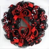 Black mesh wreath with red and white accented ribbons, with a red monogram in the center